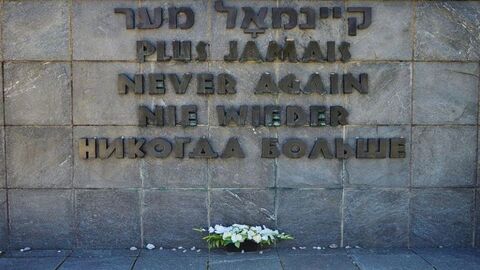 Gedenktafel, auf der in fünf Sprachen "NIE WIEDER" steht, darunter ein Blumengesteck